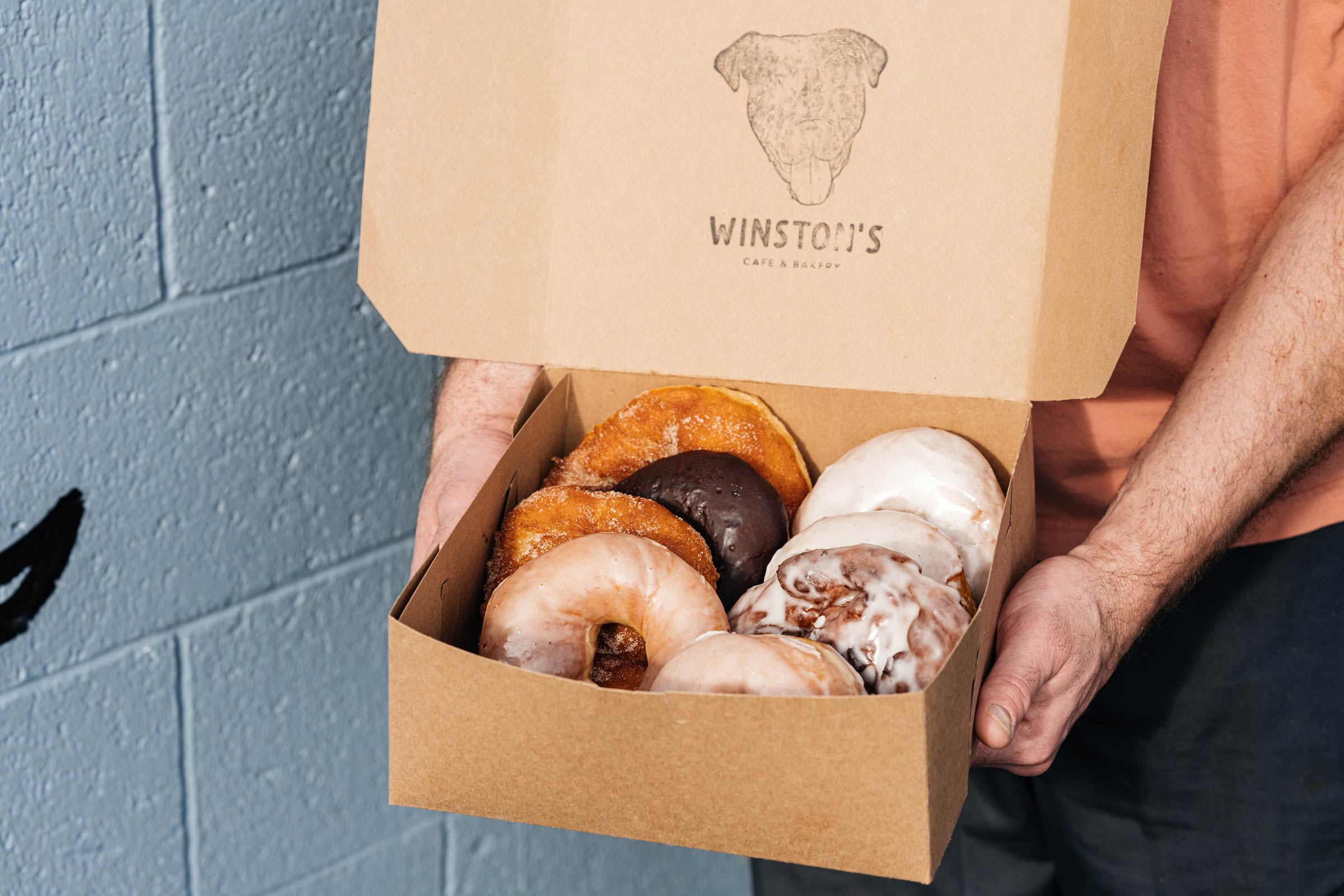 hands holding a box of doughnuts with the Winston's logo