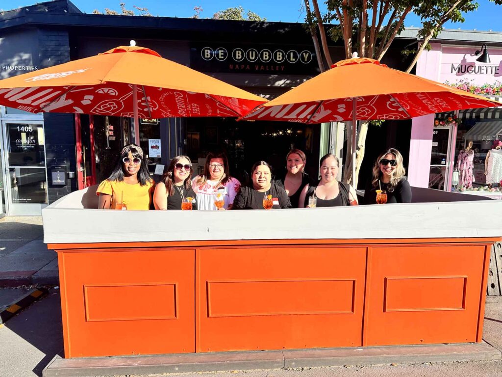 group of women seated at the Be Bubbly parklet under orange umbrellas